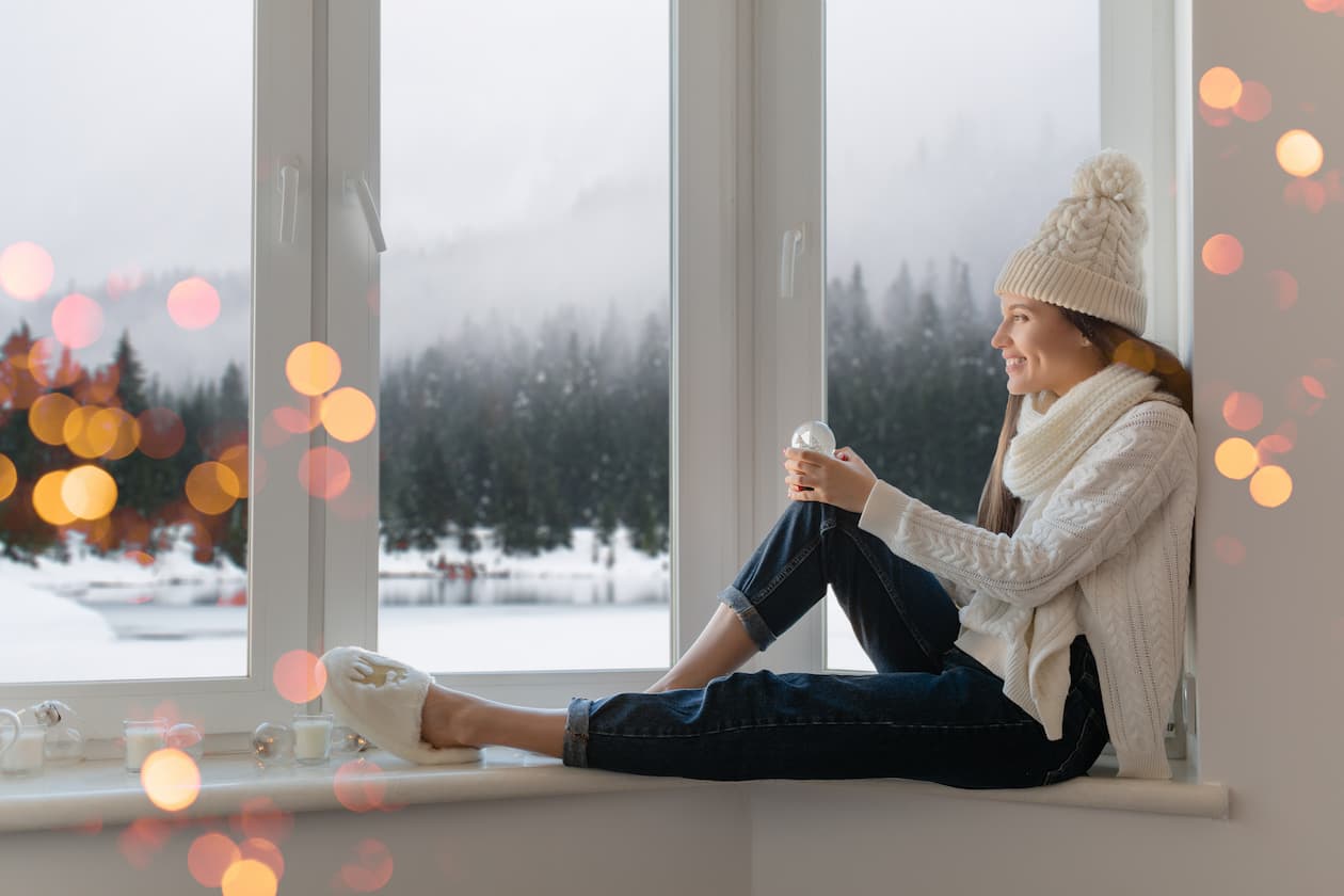 mujer sonriente aislada del frio por la ventana fuera nieve